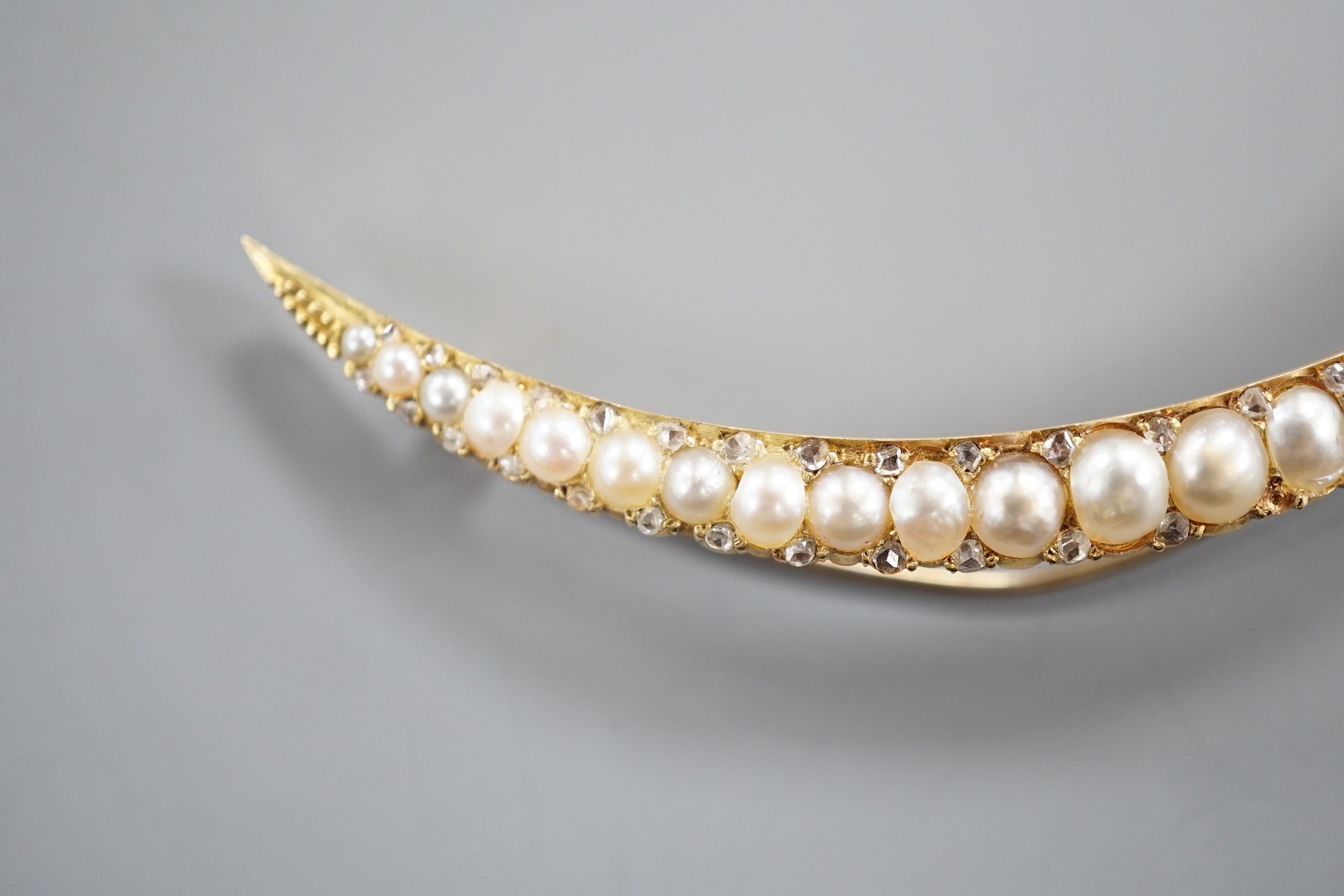 An early 20th century yellow metal and graduated split pearl set crescent brooch, with diamond chip spacers, 8cm, gross weight 8.1 grams.